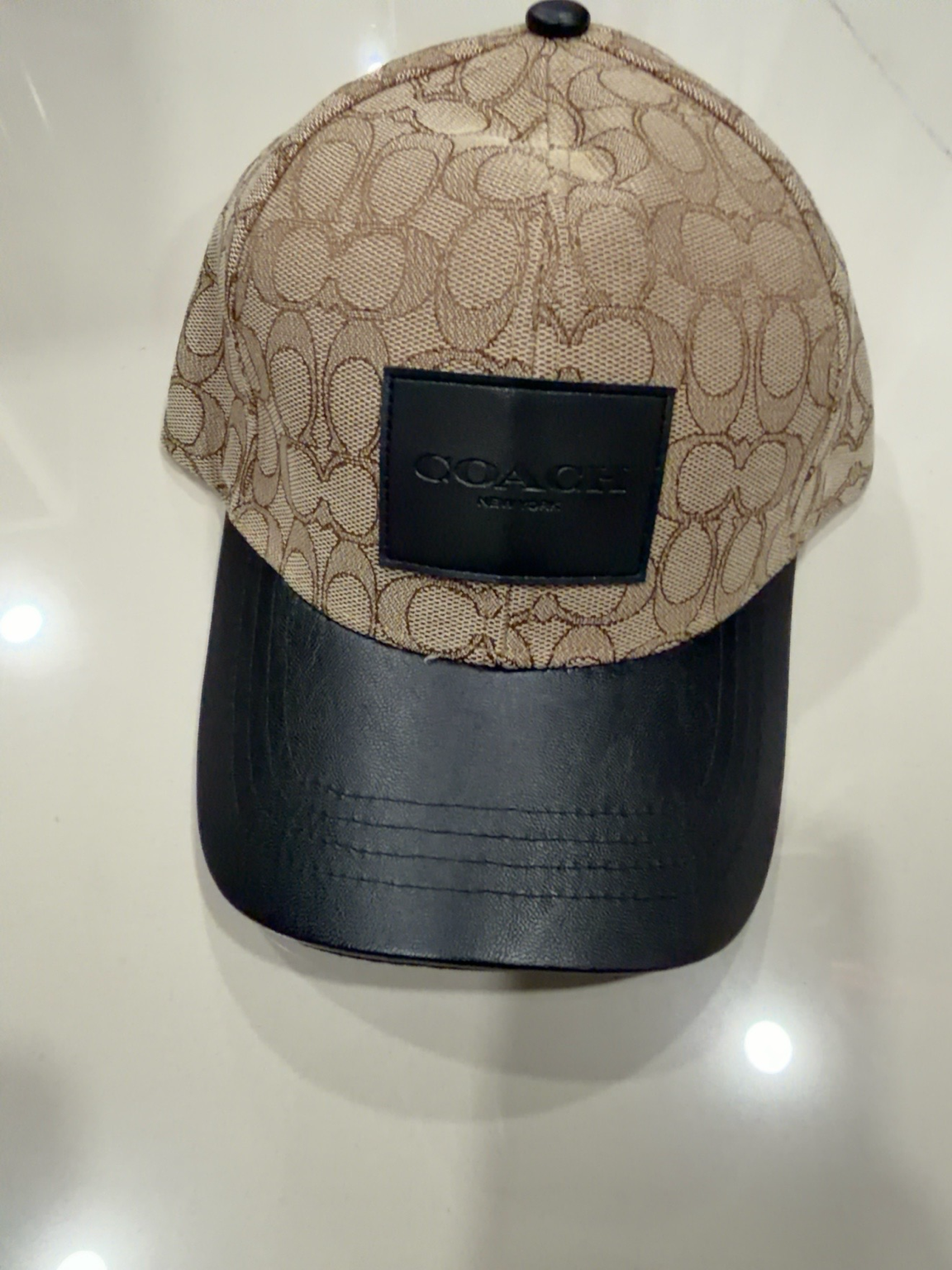 Coach beige con patrón, parche negro y visera negra tipo cuero