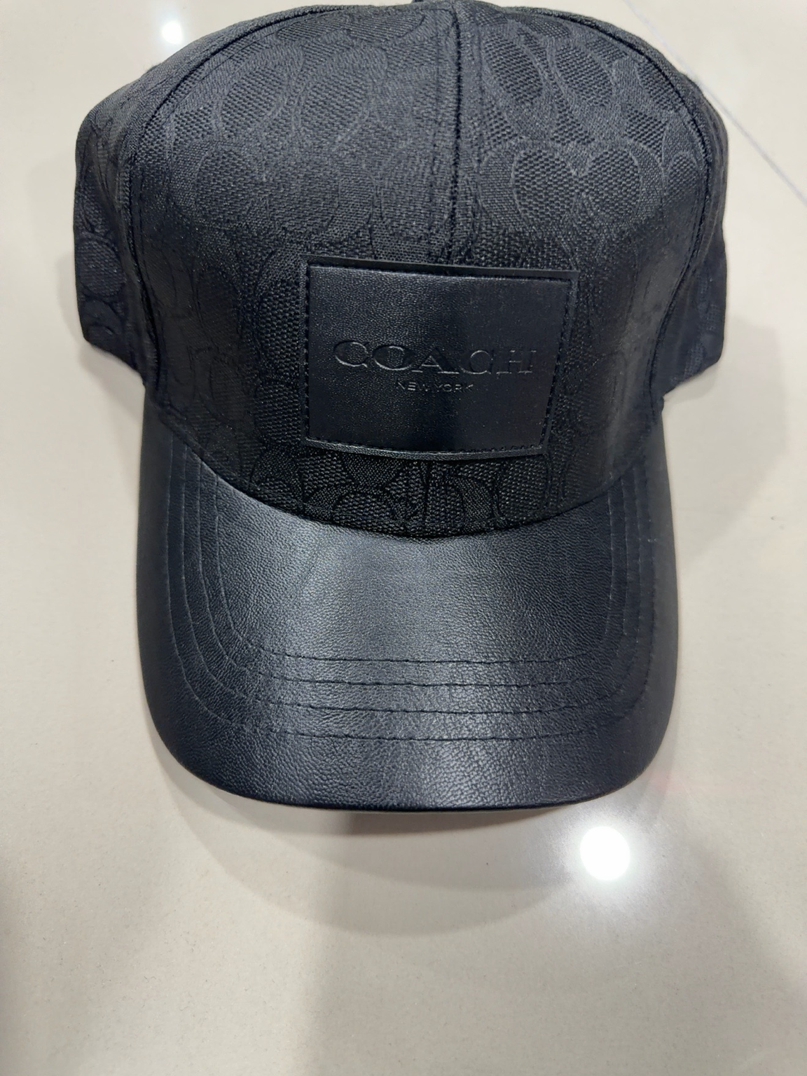 Coach negra con patrón, parche negro y visera tipo cuero