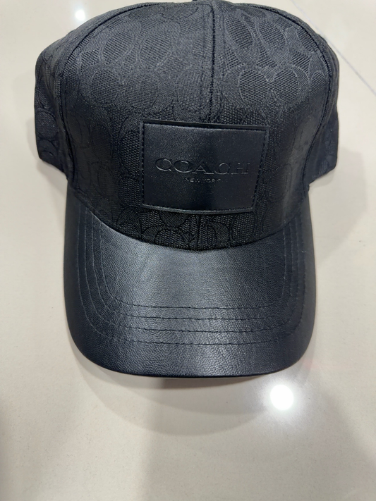 Coach negra con patrón, parche negro y visera tipo cuero